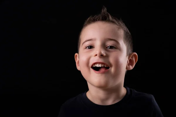 Retrato de un joven niño alegre expresión sonriente, sobre un fondo negro en casa, interior. — Foto de Stock