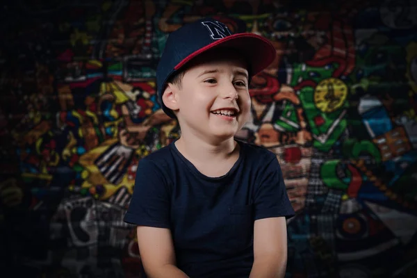 Pequeño niño feliz con una gorra azul sonriendo sobre fondo de graffiti — Foto de Stock