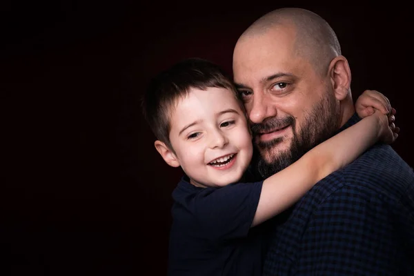 Portrait bearded father and son smile for camera on black background