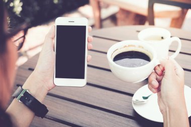 Kafede boş ekranlı akıllı telefonu tutan kadın. kırpma yolu.