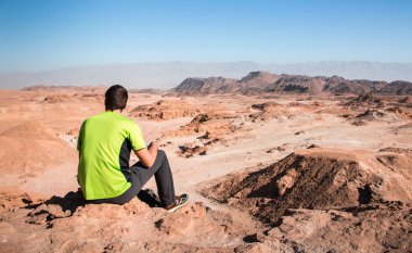 Dağın tepesinde oturan genç bir adam. Mutluluk ve özgürlük kavramı. Timna parkında yürüyüş, Negev çölü, İsrail