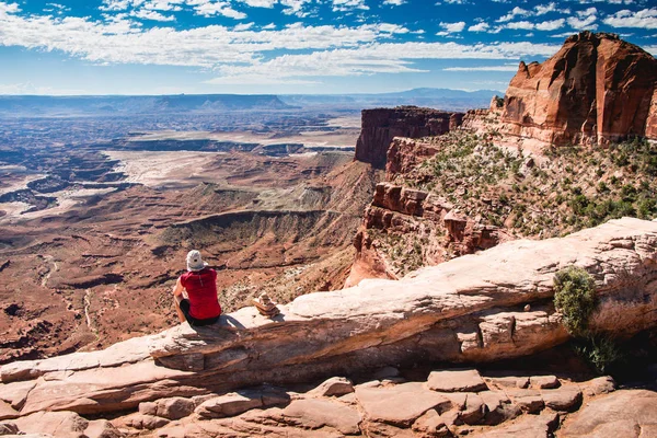 Mesa Arch yakınlarındaki Canyonlands Milli Parkı'nda kenarında oturan genç turist adam