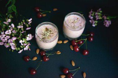 İki bardak güzel smoothies ile fındık ve çiçekler siyah bir arka plan ile. Yukarıdan görüntülemek