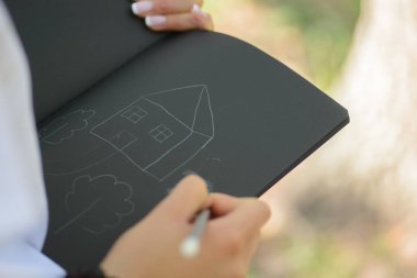 Kadının elinde bir defter boyalı evi