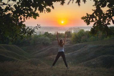 Gün batımında yoga yapan genç bir kadın. 