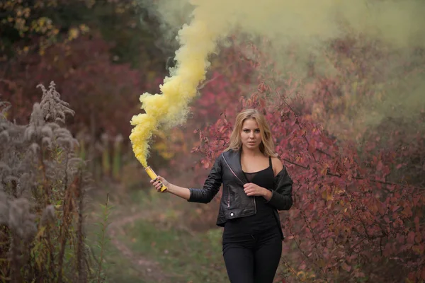 Young girl with a yellow smoke bomb on an autumn background