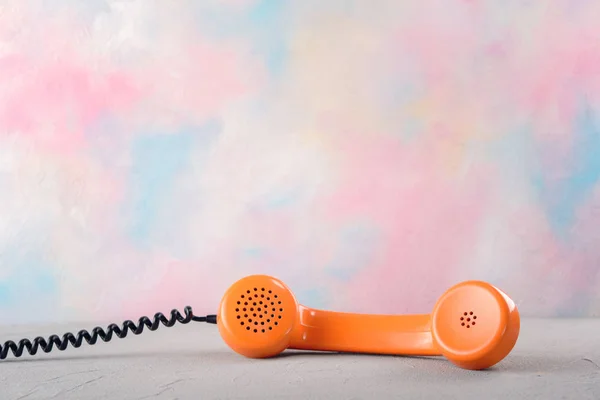 Vintage orange telephone receiver on color bright background.