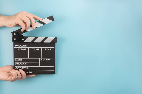 Movie clapperboard in hands on a blue background