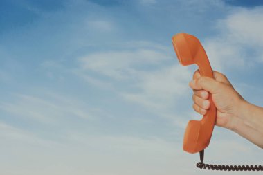 Mavi gökyüzüne karşı tutulan turuncu eski telefon ahizesi