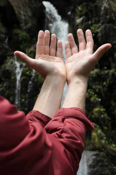 Hands raised towards a waterfall. — Stock Photo, Image