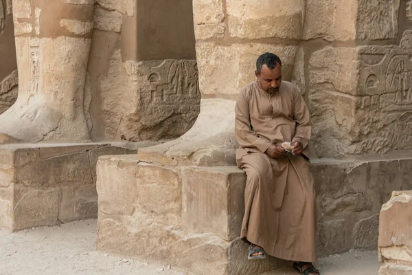 Bir adam Karnak tapınağının sütunlarında oturan para sayar. — Stok fotoğraf