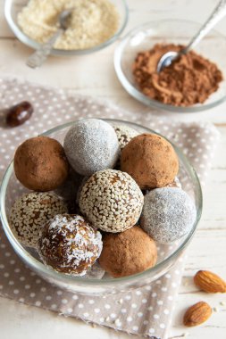 Beyaz arka planda cam bir kasede kakao ve susam tohumlu enerji topları.