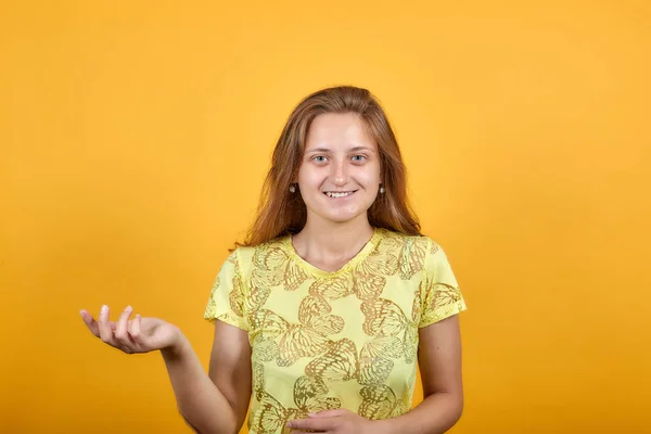 Chica morena en camiseta amarilla sobre fondo naranja aislado muestra emociones —  Fotos de Stock