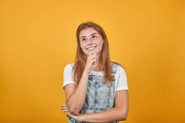 Beyaz tişört giyen genç kadın, turuncu arka plan üzerinde duygularını gösterir