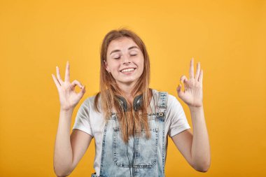 Beyaz tişört giyen genç kadın, turuncu arka plan üzerinde duygularını gösterir