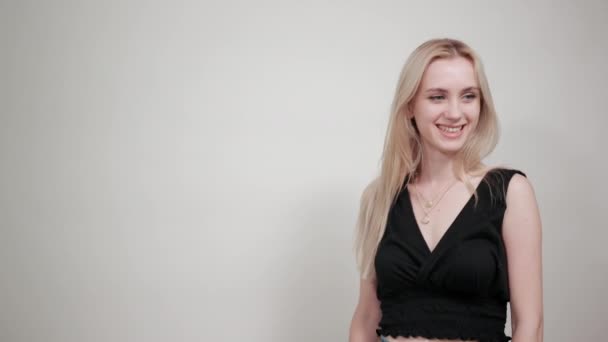 Blond meisje in een zwarte jurk over geïsoleerde witte achtergrond toont emoties — Stockvideo
