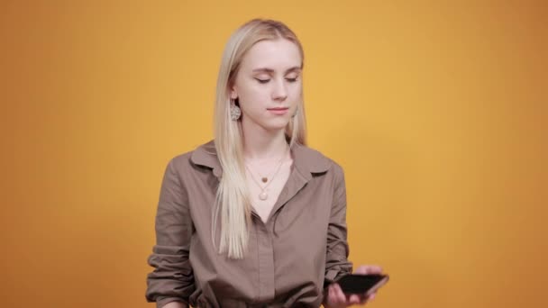 Blonde fille en chemisier brun sur fond orange isolé montre des émotions — Video