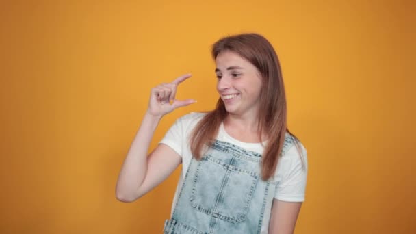 Молодая женщина в белой футболке, на оранжевом фоне показывает эмоции — стоковое видео
