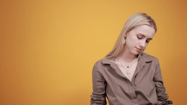 Blond meisje in bruine blouse over geïsoleerde oranje achtergrond toont emoties — Stockvideo