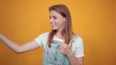 Beyaz tişört giyen genç kadın, turuncu arka plan üzerinde duygularını gösterir