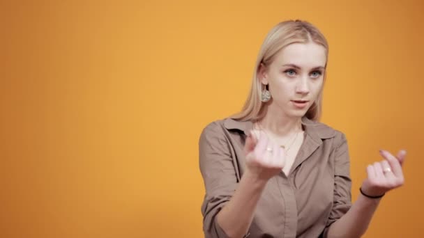 Blonde girl in brown blouse over isolated orange background shows emotions — Stock Video