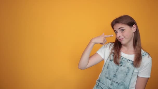 Mujer joven vistiendo camiseta blanca, sobre fondo naranja muestra emociones — Vídeos de Stock