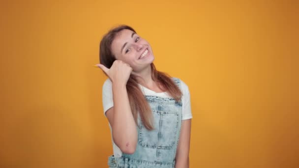 Молодая женщина в белой футболке, на оранжевом фоне показывает эмоции — стоковое видео