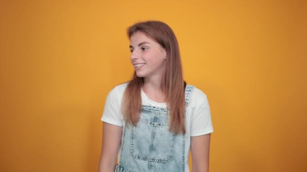 Jeune femme portant un t-shirt blanc, sur fond orange montre des émotions — Video