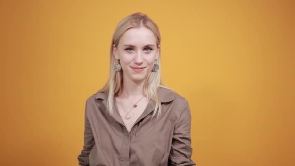 Blond meisje in bruine blouse over geïsoleerde oranje achtergrond toont emoties — Stockvideo
