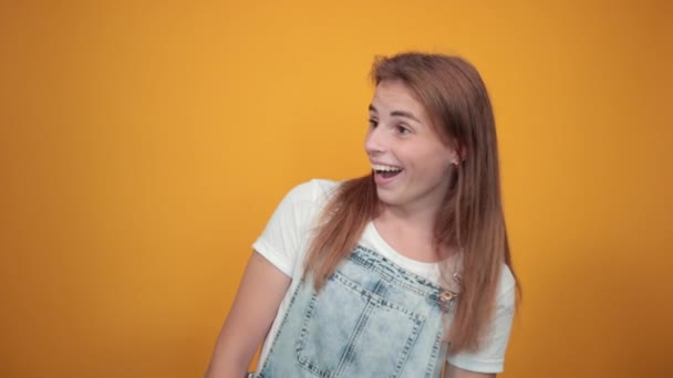 Mujer joven vistiendo camiseta blanca, sobre fondo naranja muestra emociones — Vídeos de Stock