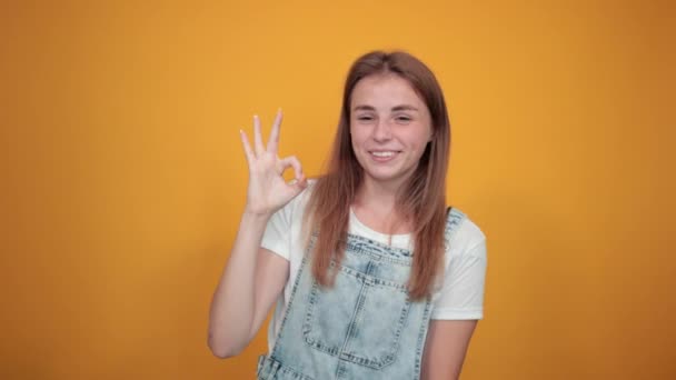 Jovem mulher vestindo camiseta branca, sobre fundo laranja mostra emoções — Vídeo de Stock