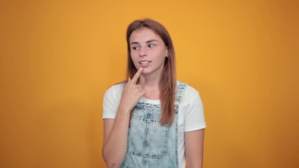 Beyaz tişört giyen genç kadın, turuncu arka plan üzerinde duygularını gösterir — Stok video