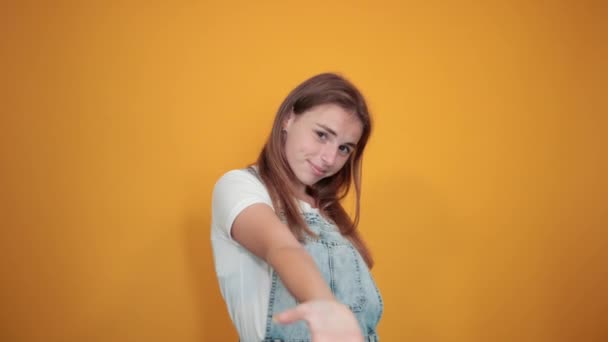 Mujer joven vistiendo camiseta blanca, sobre fondo naranja muestra emociones — Vídeo de stock