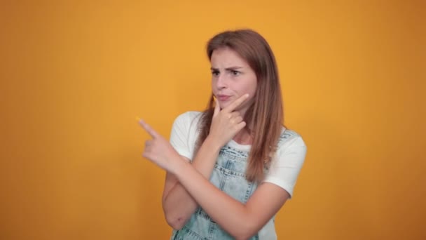 Mujer joven vistiendo camiseta blanca, sobre fondo naranja muestra emociones — Vídeo de stock