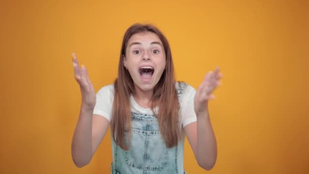 Mujer joven vistiendo camiseta blanca, sobre fondo naranja muestra emociones — Vídeo de stock