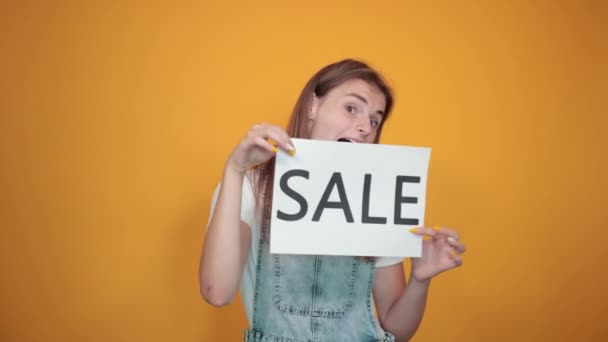 Beyaz tişört giyen genç kadın, turuncu arka plan üzerinde duygularını gösterir — Stok video