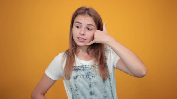 Mujer joven vistiendo camiseta blanca, sobre fondo naranja muestra emociones — Vídeos de Stock