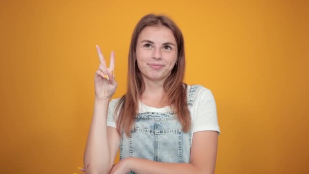 白いTシャツを着た若い女性、オレンジ色の背景に感情を示す — ストック動画