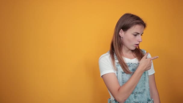 Mujer joven vistiendo camiseta blanca, sobre fondo naranja muestra emociones — Vídeo de stock