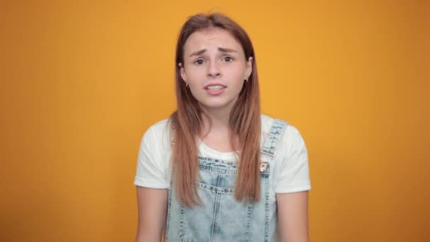 Mujer joven vistiendo camiseta blanca, sobre fondo naranja muestra emociones — Vídeos de Stock