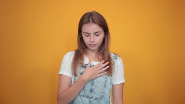 흰색 티셔츠를 입은 젊은 여성이 주황색 배경 위에 감정을 보여줍니다. — 비디오