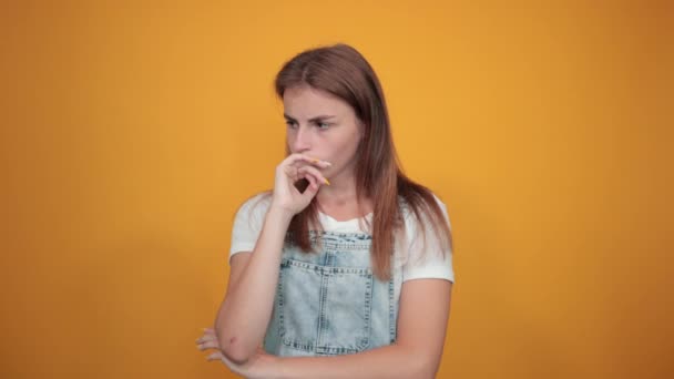 Jonge vrouw draagt wit t-shirt, over oranje achtergrond toont emoties — Stockvideo