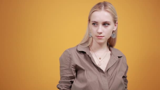 Блондинка в коричневій блузці над ізольованим помаранчевим тлом показує емоції — стокове відео