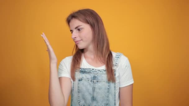 Junge Frau trägt weißes T-Shirt, über orangefarbenem Hintergrund zeigt Emotionen — Stockvideo
