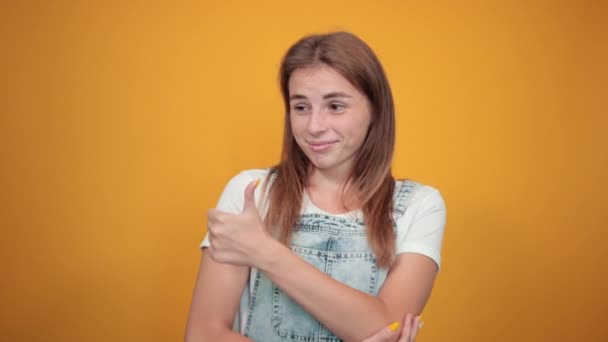 Jeune femme portant un t-shirt blanc, sur fond orange montre des émotions — Video