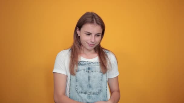 Mladá žena na bílém tričku, nad oranžovým pozadím vykazuje emoce — Stock video