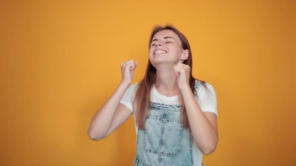 Mujer joven vistiendo camiseta blanca, sobre fondo naranja muestra emociones — Vídeo de stock