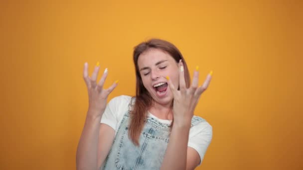 Young woman wearing white t-shirt, over orange background shows emotions — Stock Video