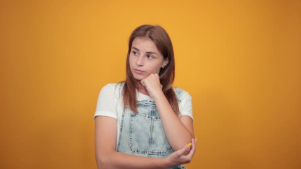 Jonge vrouw draagt wit t-shirt, over oranje achtergrond toont emoties — Stockvideo