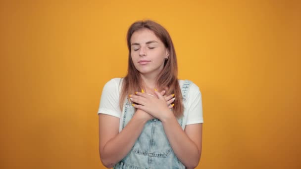 Fiatal nő visel fehér póló, több mint narancssárga háttér mutatja érzelmek — Stock videók